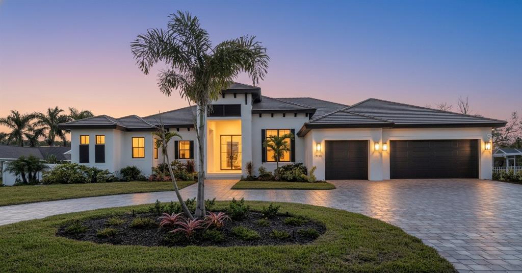 A modern single-story house with a paved driveway, palm tree, and dark garage doors at dusk — 7125 WESTMORELAND DRIVE, SARASOTA, FL