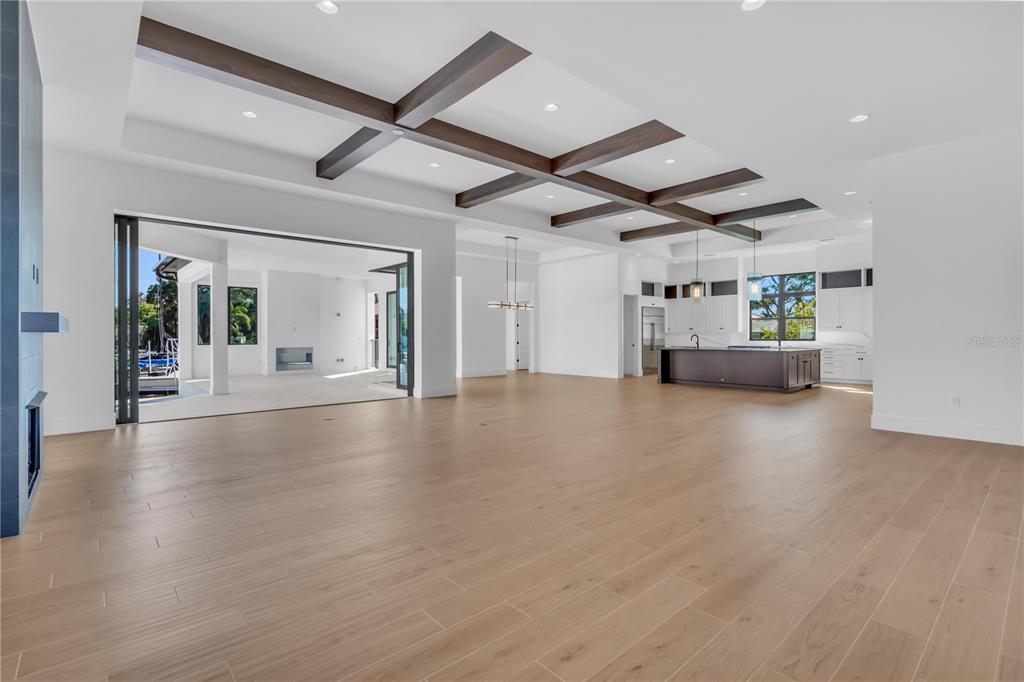 An open-concept living area features light wood flooring, a coffered ceiling with beams, and sliding doors — 7125 WESTMORELAND DRIVE, SARASOTA, FL
