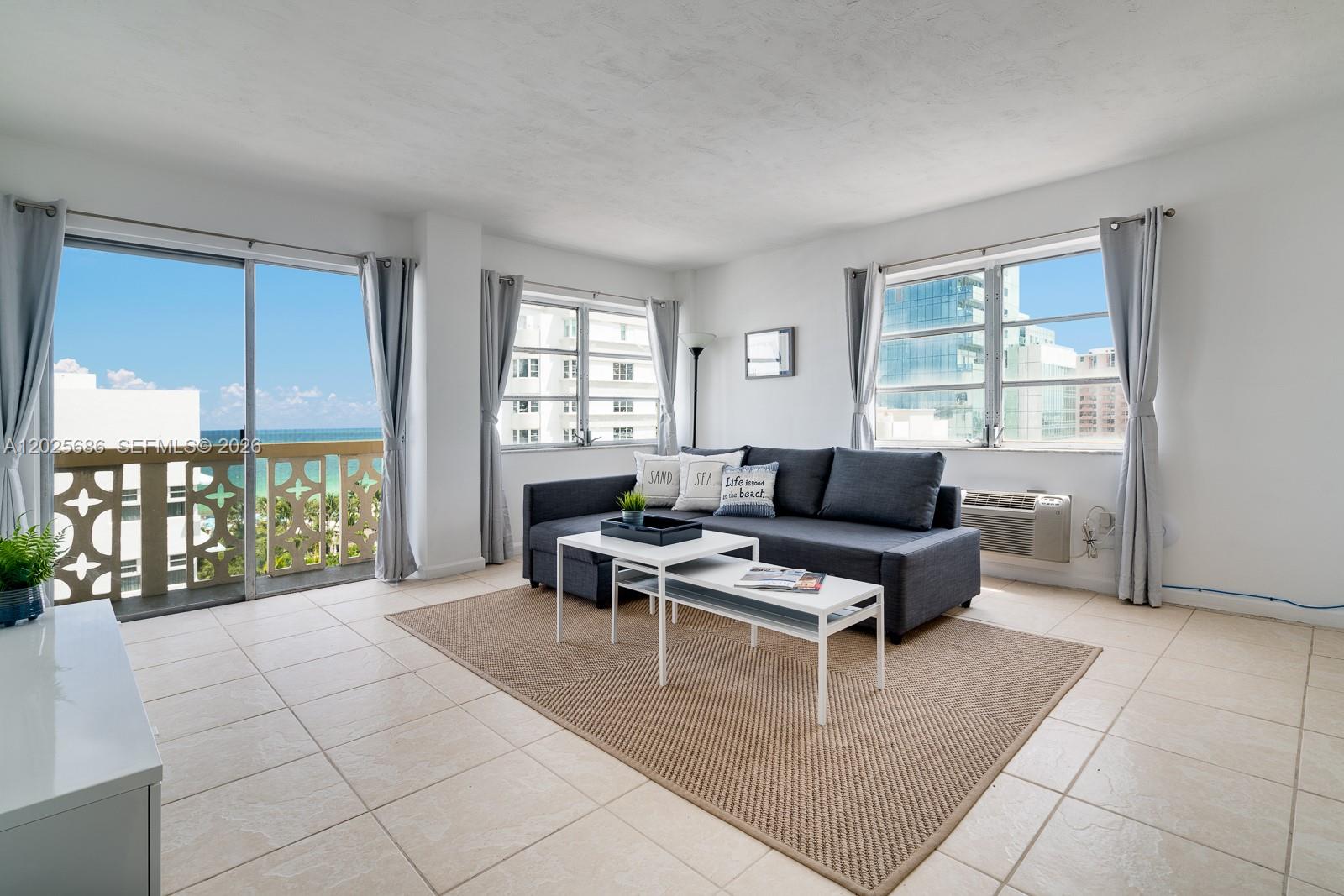 A living room features a dark sofa, white coffee tables, tile floors, and a balcony view — 3100 Collins Ave # 1101, Miami Beach FL 33140, MIAMI BEACH, FL