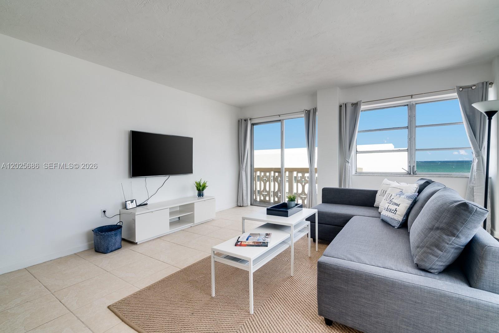 A living room features a gray sectional sofa, white media console, and ocean views — 3100 Collins Ave # 1101, Miami Beach FL 33140, MIAMI BEACH, FL