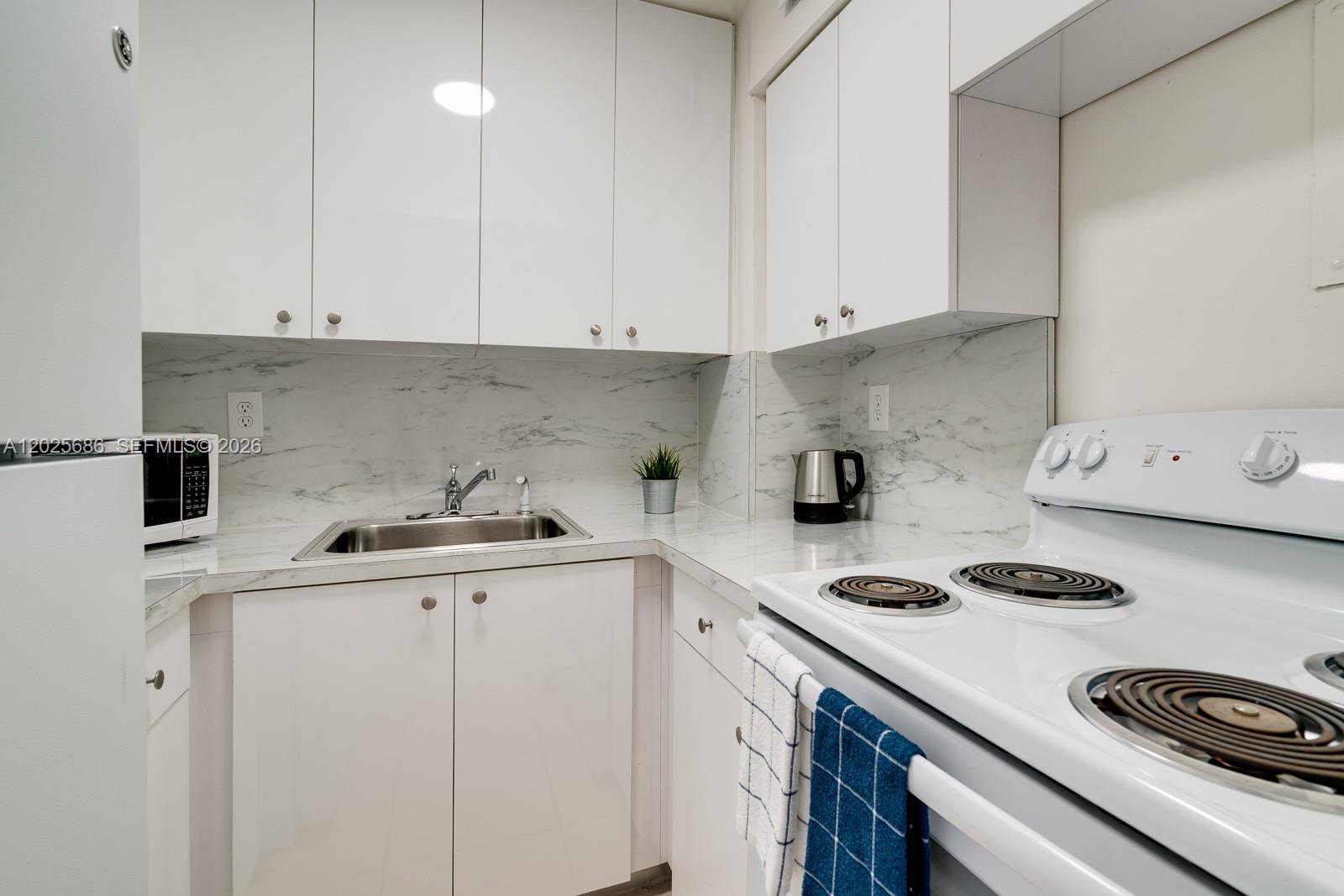 A small kitchen features white cabinets, marble-patterned countertops, and a white electric stove — 3100 Collins Ave # 1101, Miami Beach FL 33140, MIAMI BEACH, FL