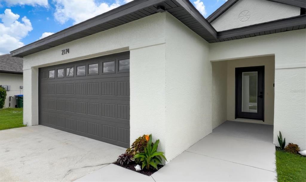 A white stucco house exterior features a dark gray garage door and a front entryway — 2174 BRUBECK ROAD, NORTH PORT, FL