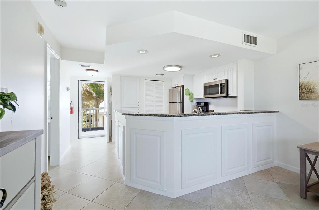 A white kitchen with a granite-topped peninsula, stainless steel appliances, and tile flooring — 5000 GASPARILLA ROAD UNIT BC205, BOCA GRANDE, FL