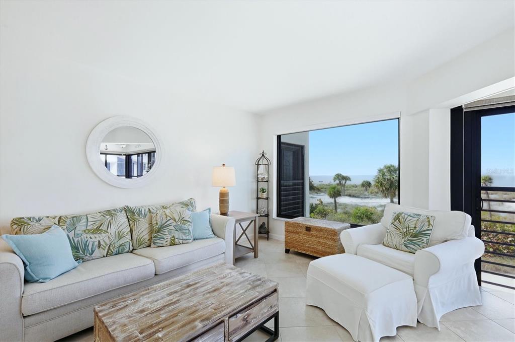A bright living room features a sofa, armchair, ottoman, and large window with ocean views — 5000 GASPARILLA ROAD UNIT BC205, BOCA GRANDE, FL