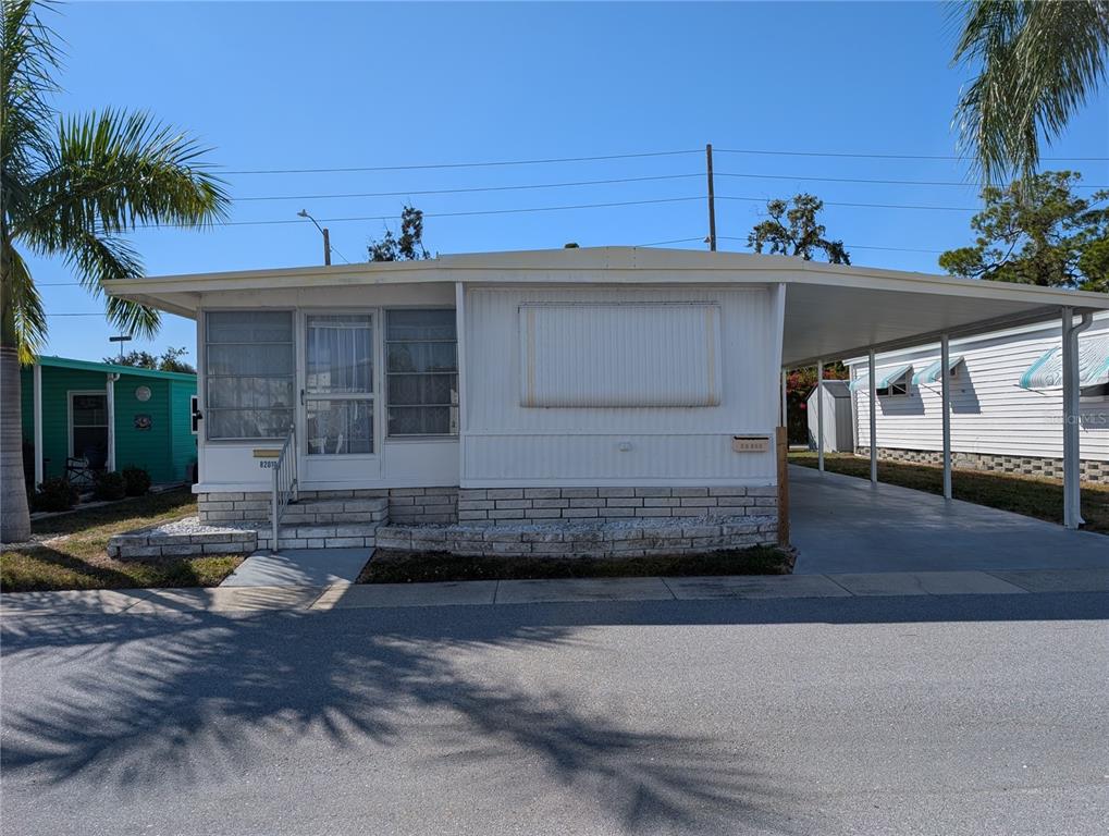 A white mobile home features a screened-in front porch, a carport, and a brick foundation — 82010 A STREET N UNIT 10, PINELLAS PARK, FL
