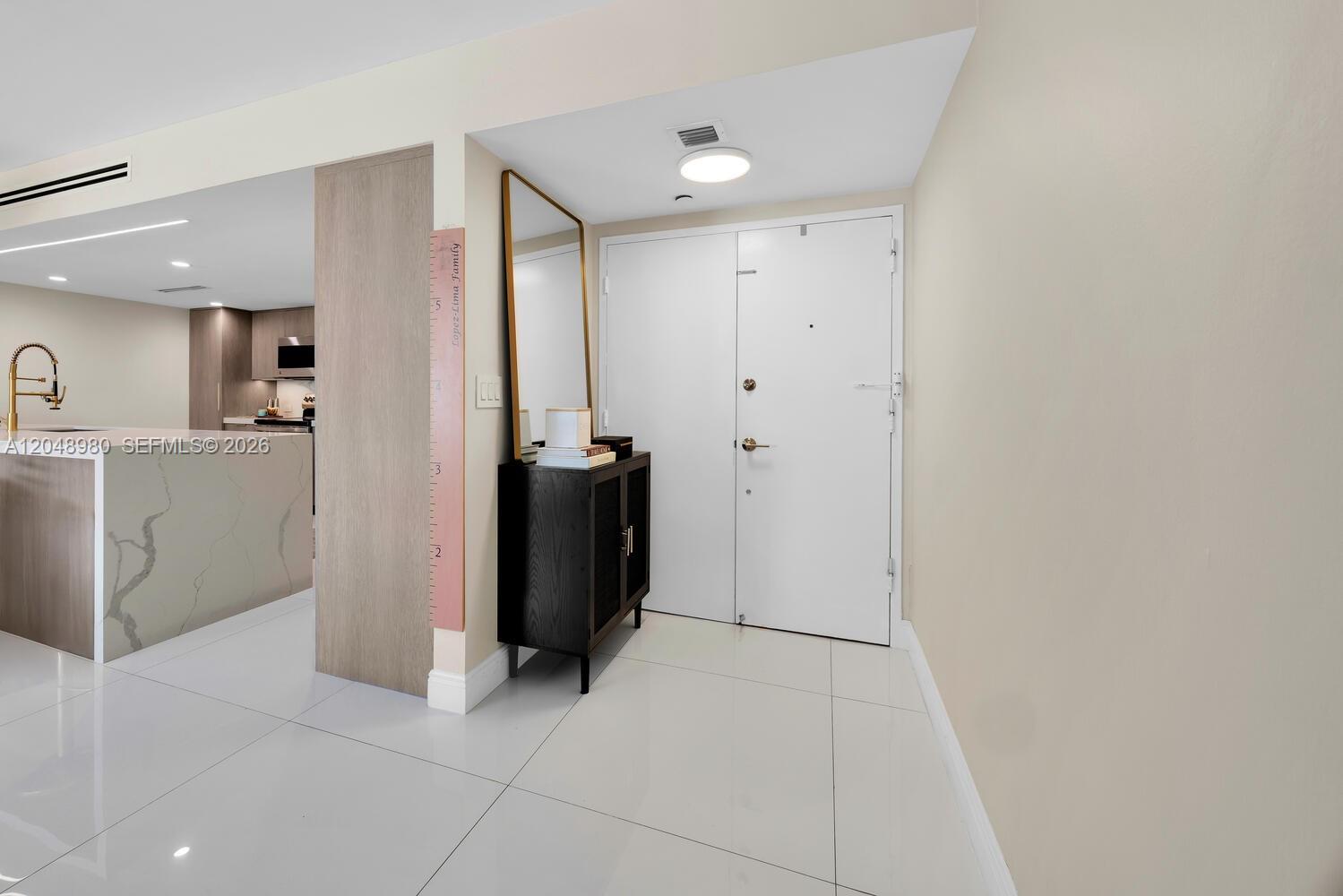 An entryway features white tile floors, a black cabinet, a tall mirror, and a white door — 155 Ocean Lane Dr # 413, Key Biscayne FL 33149, KEY BISCAYNE, FL