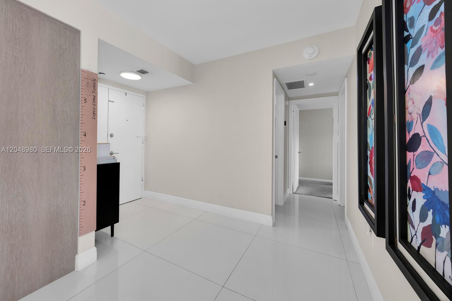 A bright hallway features white tile floors, neutral walls, and framed floral artwork — 155 Ocean Lane Dr # 413, Key Biscayne FL 33149, KEY BISCAYNE, FL