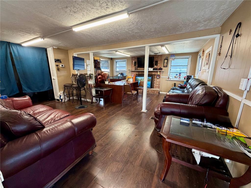 A living room features dark wood flooring, leather furniture, and a brick fireplace — 4131 GRAND BOULEVARD, NEW PORT RICHEY, FL