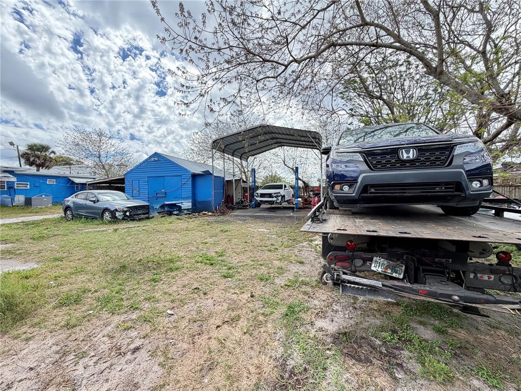 A blue Honda sits on a flatbed truck in a yard with a metal carport — 4131 GRAND BOULEVARD, NEW PORT RICHEY, FL