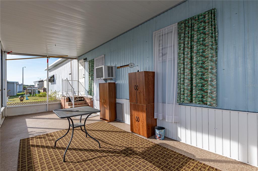 A covered patio features a metal table, a brown rug, and two wooden cabinets — 7139 EL CONQUISTADOR STREET, ZEPHYRHILLS, FL