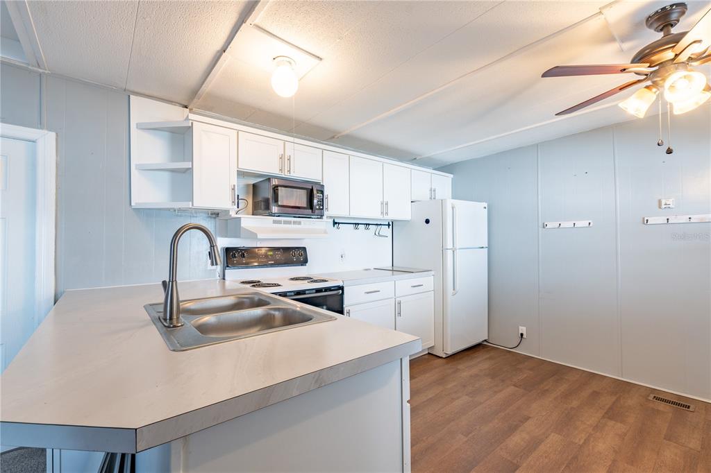 A kitchen features white cabinets, a double sink, a white refrigerator, and wood-look flooring — 7139 EL CONQUISTADOR STREET, ZEPHYRHILLS, FL