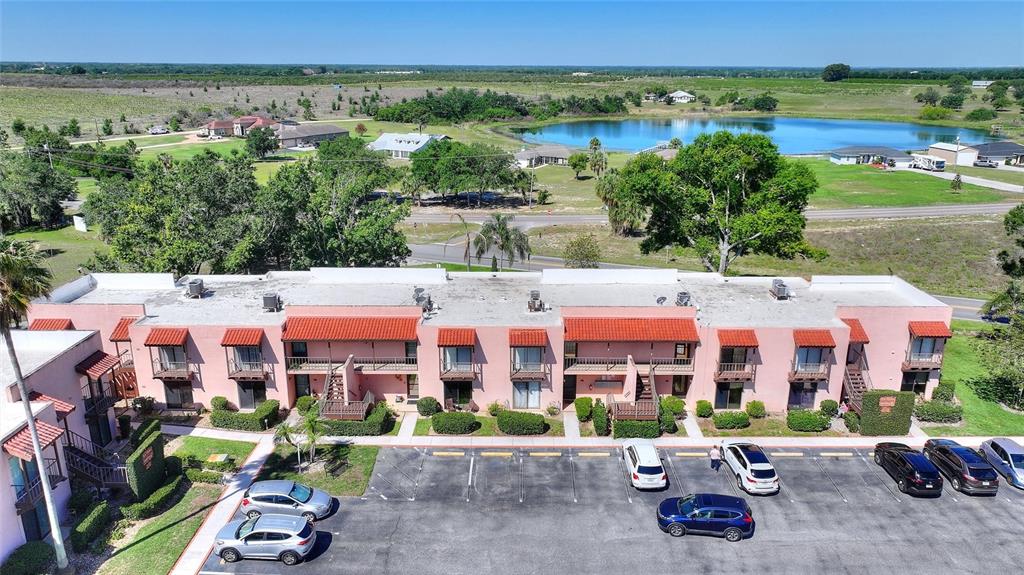 An aerial view shows a pink, two-story apartment building with a parking lot and lake — 206 LA CASA UNIT 206, LAKE WALES, FL