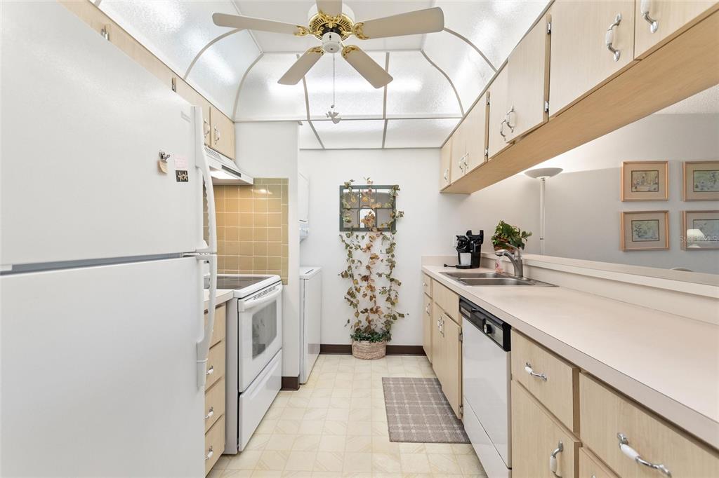 A galley kitchen features light wood cabinets, white appliances, a ceiling fan, and tiled flooring — 206 LA CASA UNIT 206, LAKE WALES, FL