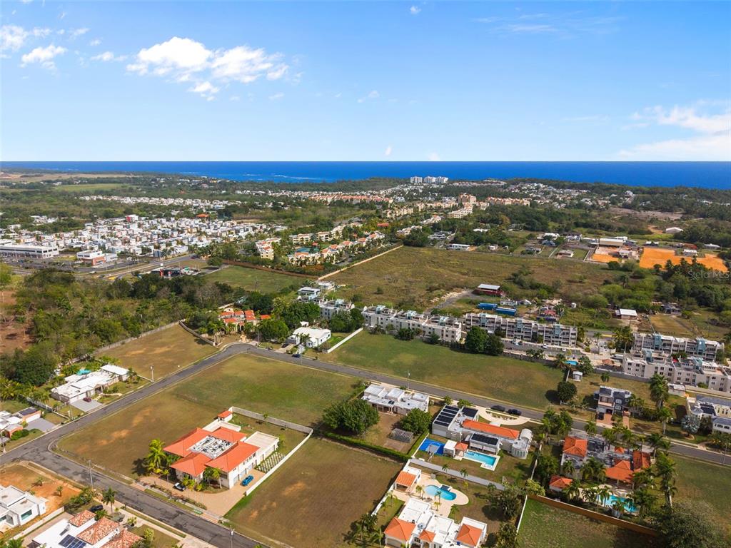 An aerial view shows a residential neighborhood with houses, apartment buildings, and undeveloped land near the ocean — G8 CALLE 2, VEGA ALTA, PR