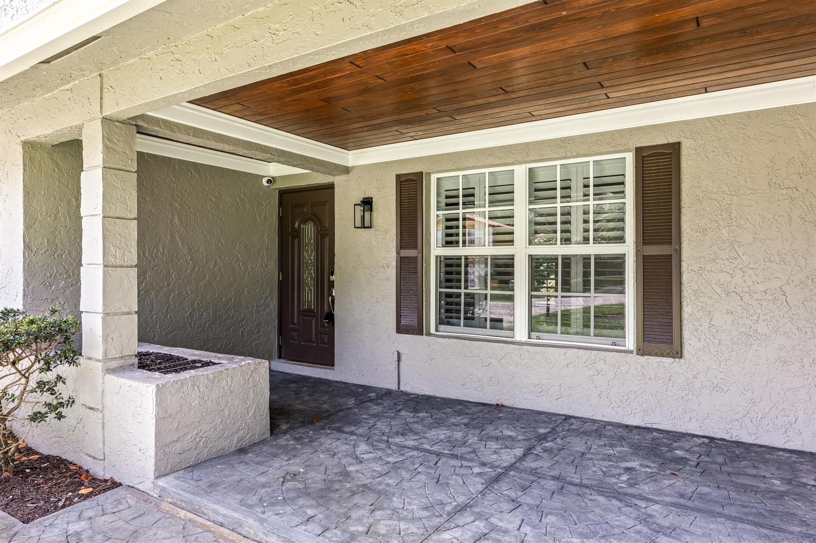 A covered front porch features a textured concrete floor, a wood-paneled ceiling, and a front door — 4610 Pinetree Drive, Delray Beach FL 33445, DELRAY BEACH, FL
