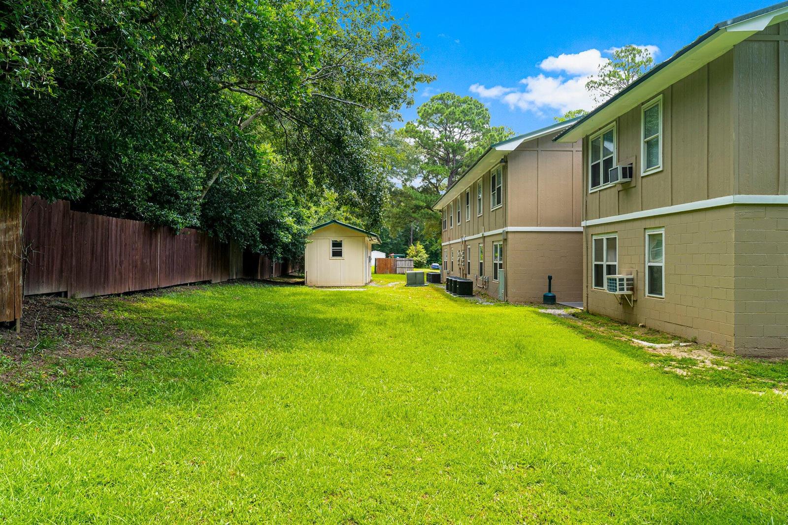 A grassy backyard area beside a multi-story apartment building with a small detached shed — 872 Deer Wood Lane, FL 32428, FL
