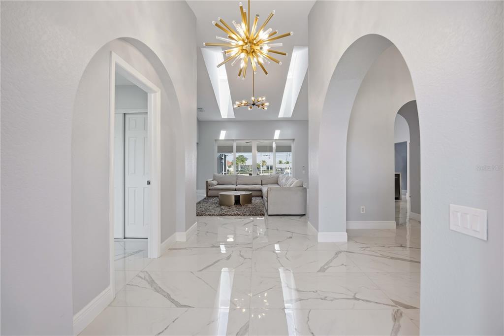 A bright entryway with arched doorways, marble-look tile flooring, and a large gold starburst chandelier — 5186 FORBES TERRACE, PORT CHARLOTTE, FL