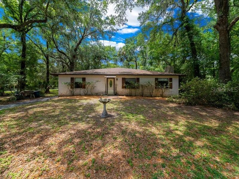 A single-story house with a light-colored exterior sits in a wooded yard — 495 & 499 N ROBIN HOOD ROAD, INVERNESS, FL