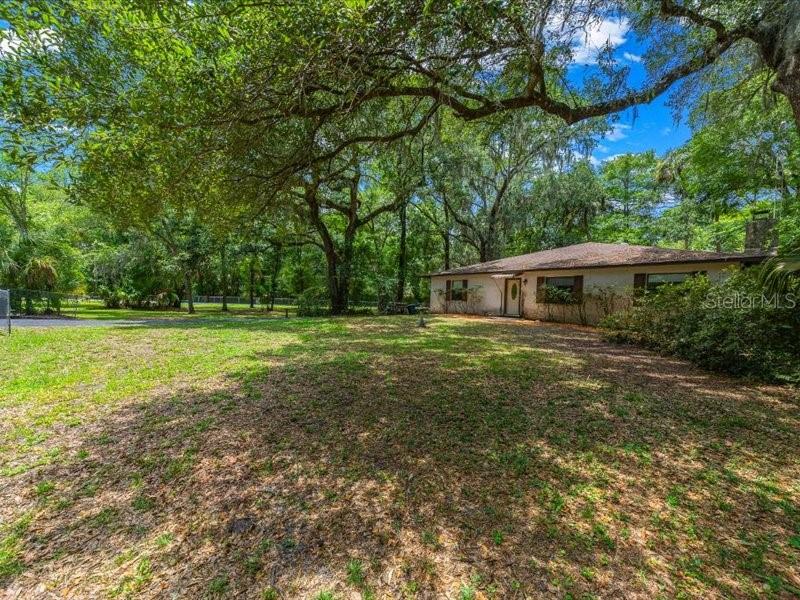 A single-story house sits on a large, tree-shaded lot with a grassy yard — 495 & 499 N ROBIN HOOD ROAD, INVERNESS, FL
