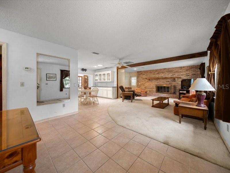 A living room with a brick fireplace, beige carpeting, and an adjacent tiled dining area — 495 & 499 N ROBIN HOOD ROAD, INVERNESS, FL