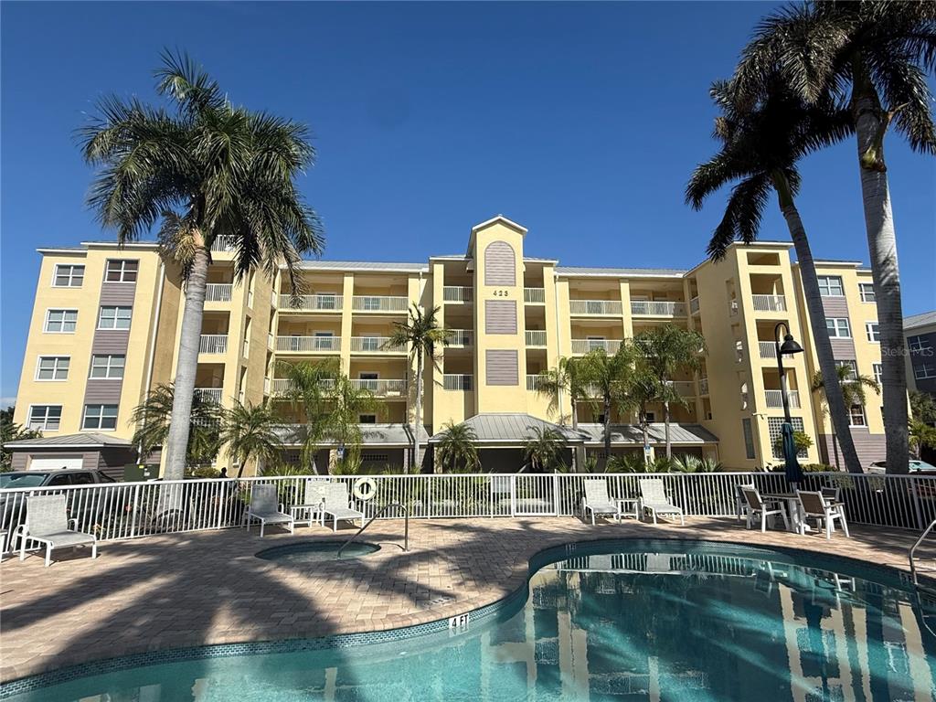 A multi-story yellow apartment building stands behind a swimming pool and white fence — 423 150TH AVENUE UNIT 1405, MADEIRA BEACH, FL