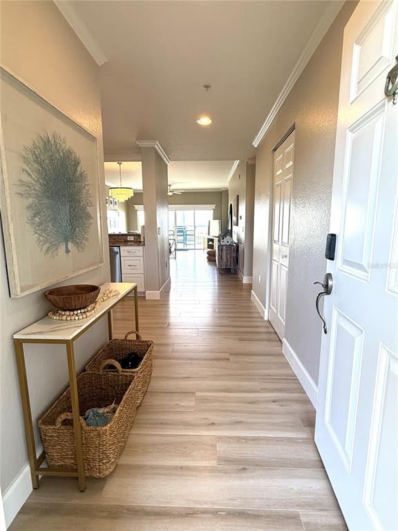 A hallway with light wood flooring leads from an entryway toward a kitchen and balcony — 423 150TH AVENUE UNIT 1405, MADEIRA BEACH, FL