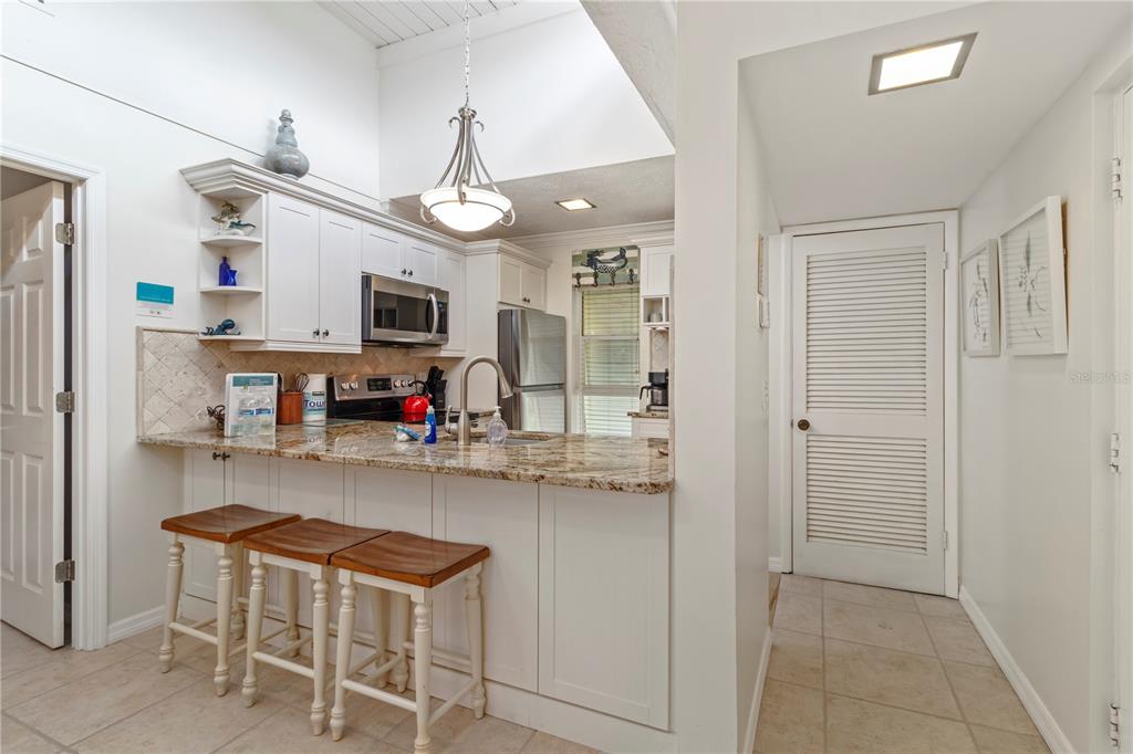 A kitchen with white cabinets, granite countertops, a breakfast bar with stools, and tile flooring — 5310 GULF OF MEXICO DRIVE UNIT 16, LONGBOAT KEY, FL