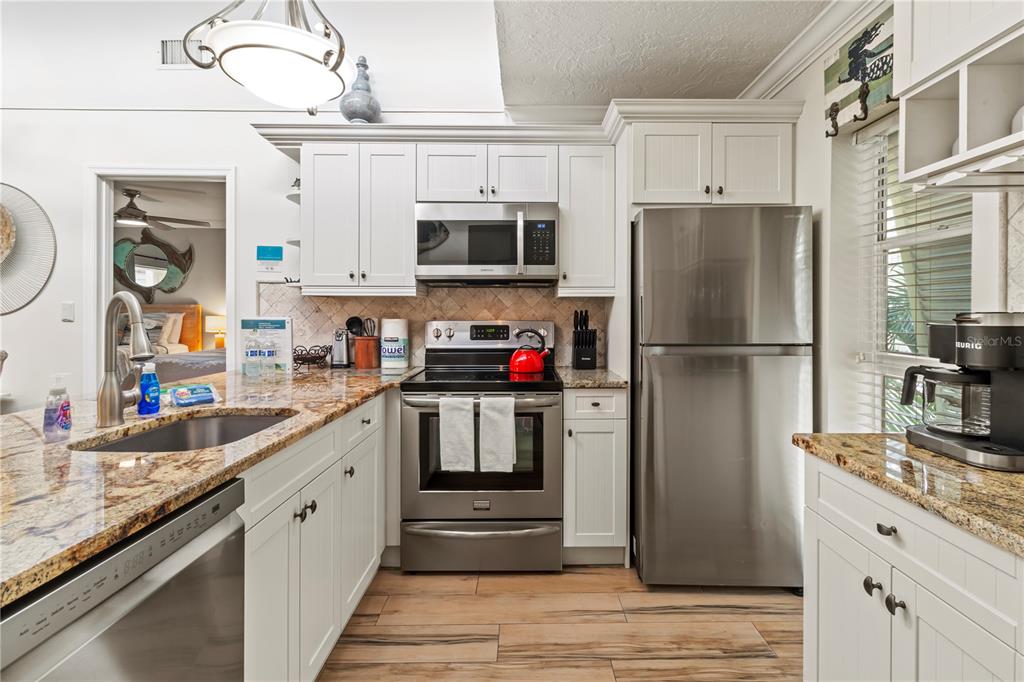 A kitchen features white cabinets, stainless steel appliances, granite countertops, and wood-look tile flooring — 5310 GULF OF MEXICO DRIVE UNIT 16, LONGBOAT KEY, FL