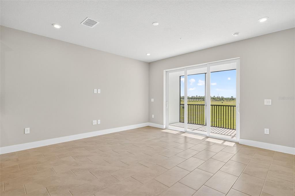 An empty room with light-colored tile flooring, recessed lighting, and a sliding glass door — 17420 MOONFLOWER DRIVE UNIT 202, VENICE, FL