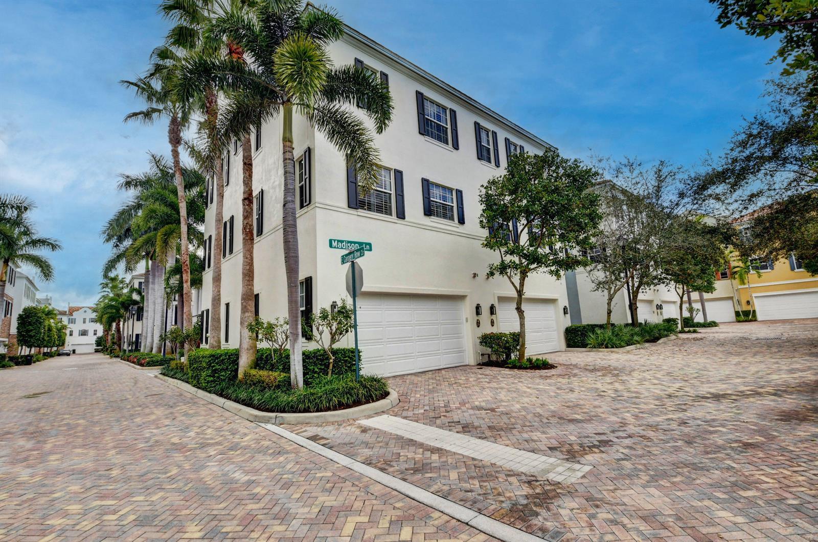 A three-story townhouse with a white exterior, two garage doors, and palm trees — 134 Madison Lane, Delray Beach FL 33444, DELRAY BEACH, FL