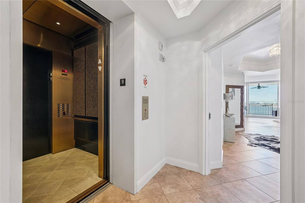 An elevator with gold-toned doors opens into a tiled hallway leading to a bright living area — 5823 BOWEN DANIEL DRIVE UNIT 902, TAMPA, FL