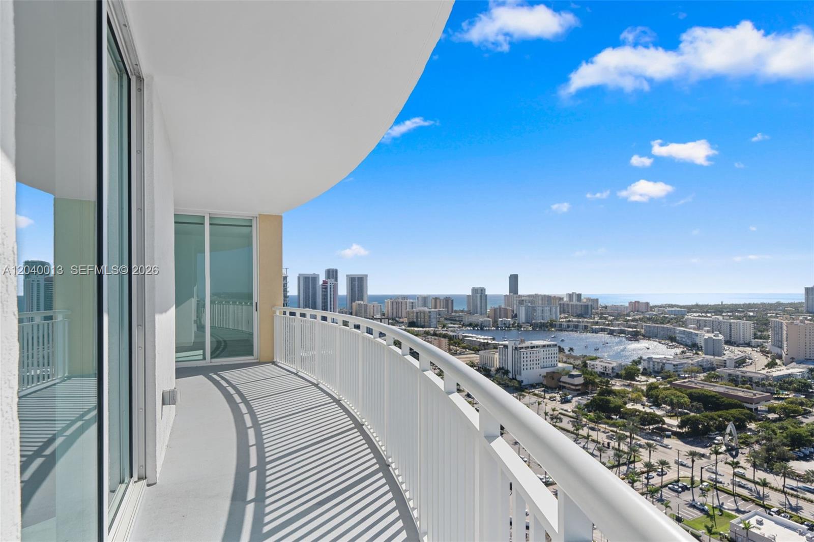 A curved balcony overlooks a coastal city skyline and a bay under a blue sky — 1745 E Hallandale Beach Blvd, Hallandale Beach FL 33009, HALLANDALE BEACH, FL