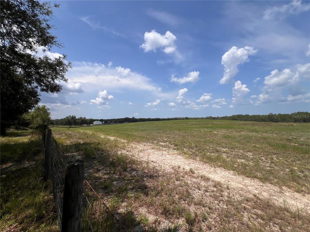 A wire fence borders a large, open grassy field under a blue sky with clouds — 5990 W OAKHILL STREET, DUNNELLON, FL