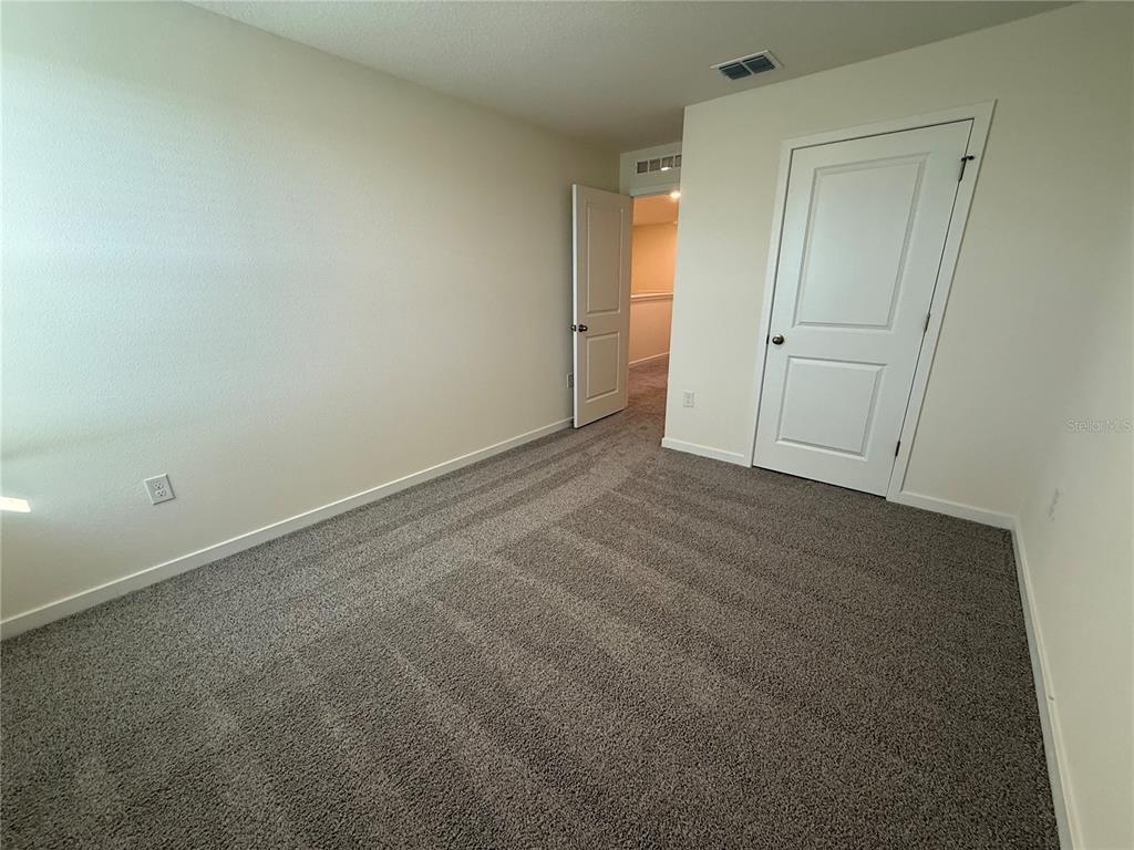 An empty bedroom features beige walls, gray carpet, and two white interior doors — 599 PRESTON COVE DRIVE, ST CLOUD, FL