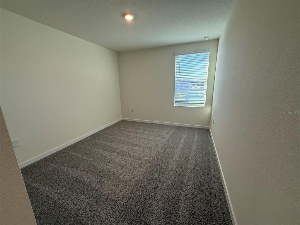 An empty bedroom features neutral walls, gray carpeting, and a single window with blinds — 599 PRESTON COVE DRIVE, ST CLOUD, FL