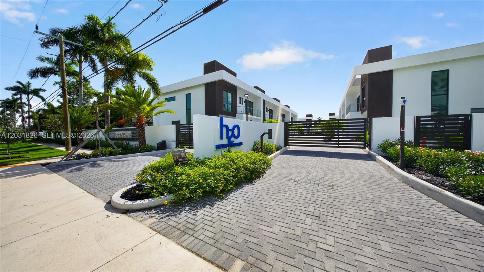A paved driveway leads to the gated entrance of a modern residential complex with palm trees — 4656 SW 32nd Ave # B1, Dania Beach FL 33312, DANIA BEACH, FL