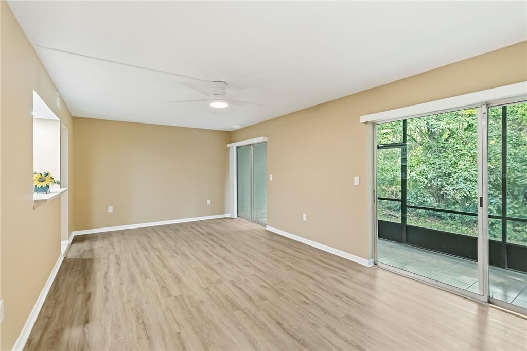 An empty living room features light wood-look flooring, beige walls, a ceiling fan, and sliding doors — 164 PERIMETER DRIVE UNIT 4A, DELTONA, FL