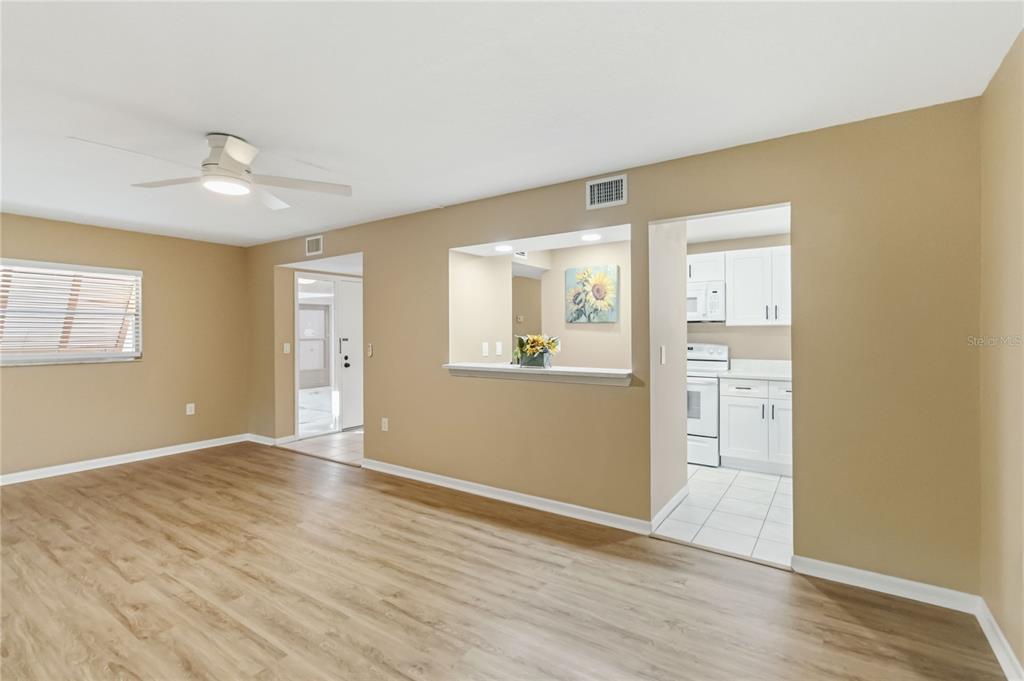 A living room with wood-look flooring, a ceiling fan, and an opening to a kitchen — 164 PERIMETER DRIVE UNIT 4A, DELTONA, FL