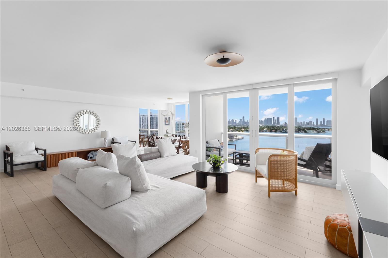 A bright living room features white furniture, light wood flooring, and a balcony with water views — 1800 Sunset Harbour # 1612, Miami Beach FL 33139, MIAMI BEACH, FL