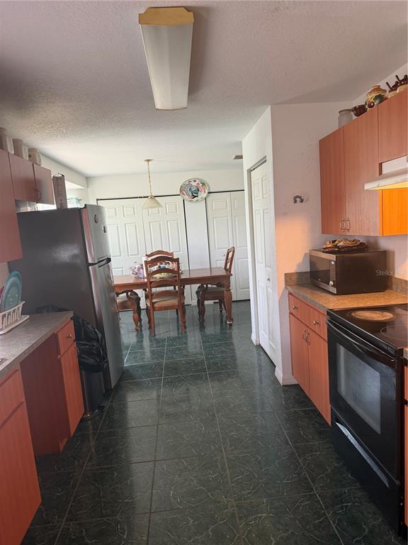 A kitchen with wood cabinets and dark green tile flooring opens to a dining area — 2135 SW 156TH PLACE, OCALA, FL