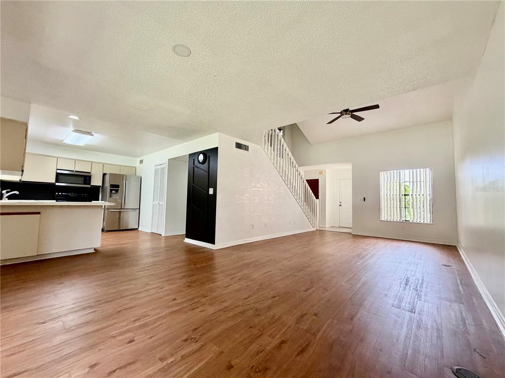 An open-concept living area with wood-look flooring, a kitchen, and a staircase — 2135 BALBOA WAY, KISSIMMEE, FL