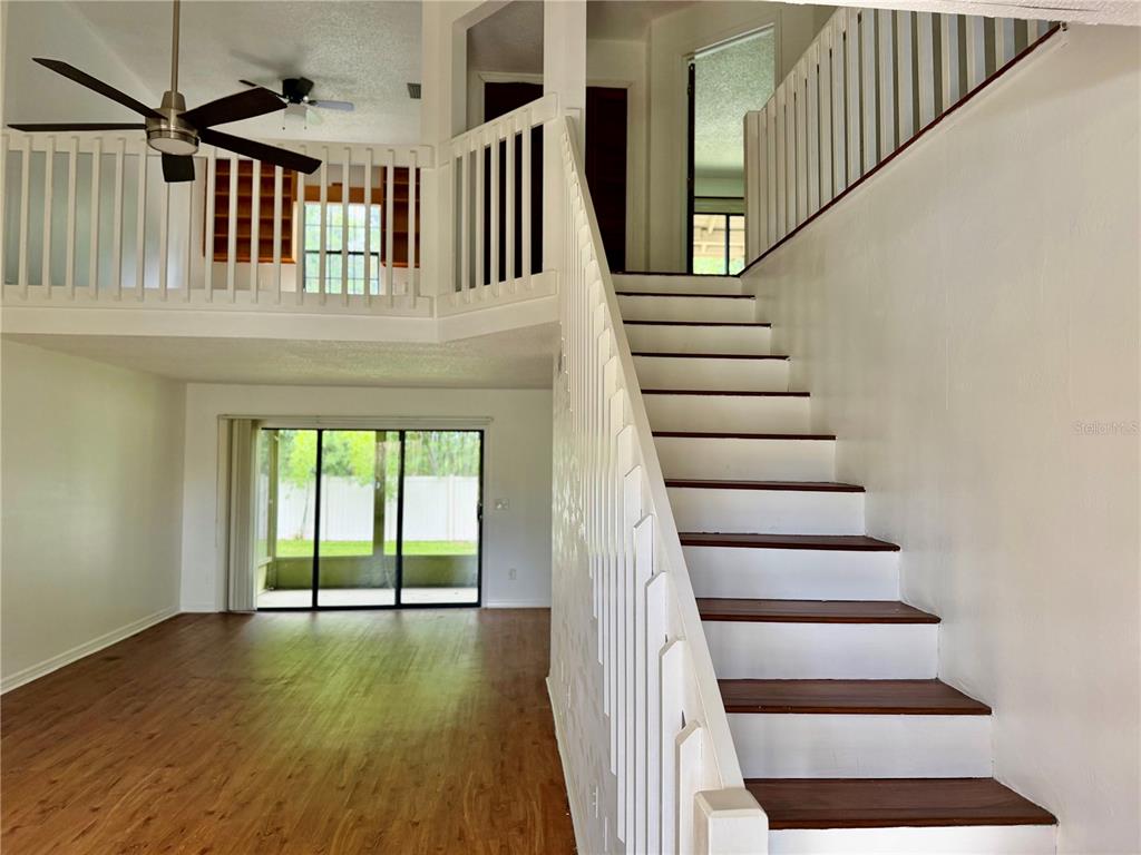 A staircase with white railings leads to an upper landing overlooking a living room area — 2135 BALBOA WAY, KISSIMMEE, FL