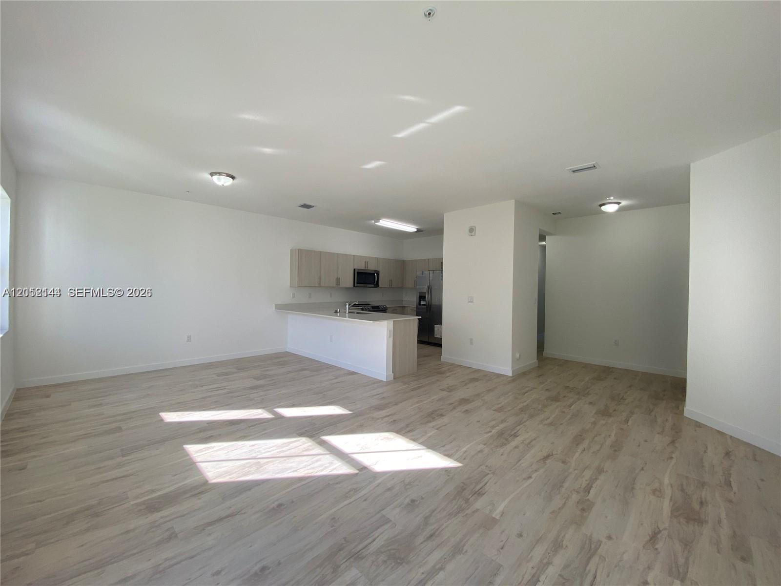 A modern kitchen features light wood cabinetry, white countertops, and an island with bar seating — 15540 SW 136th St # 105, Miami FL 33196, MIAMI, FL