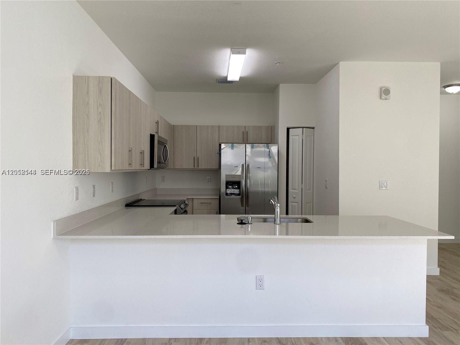 A treadmill sits in a room with light wood flooring, a console table, and a kitchen — 15540 SW 136th St # 105, Miami FL 33196, MIAMI, FL