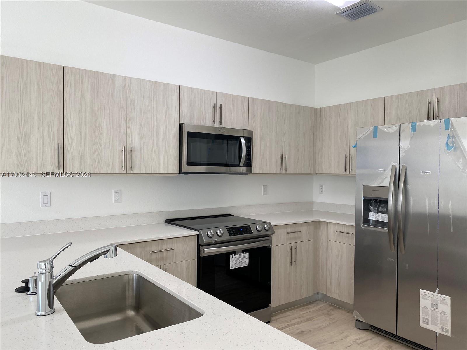 A modern kitchen features light wood cabinets, stainless steel appliances, and white quartz countertops — 15540 SW 136th St # 105, Miami FL 33196, MIAMI, FL