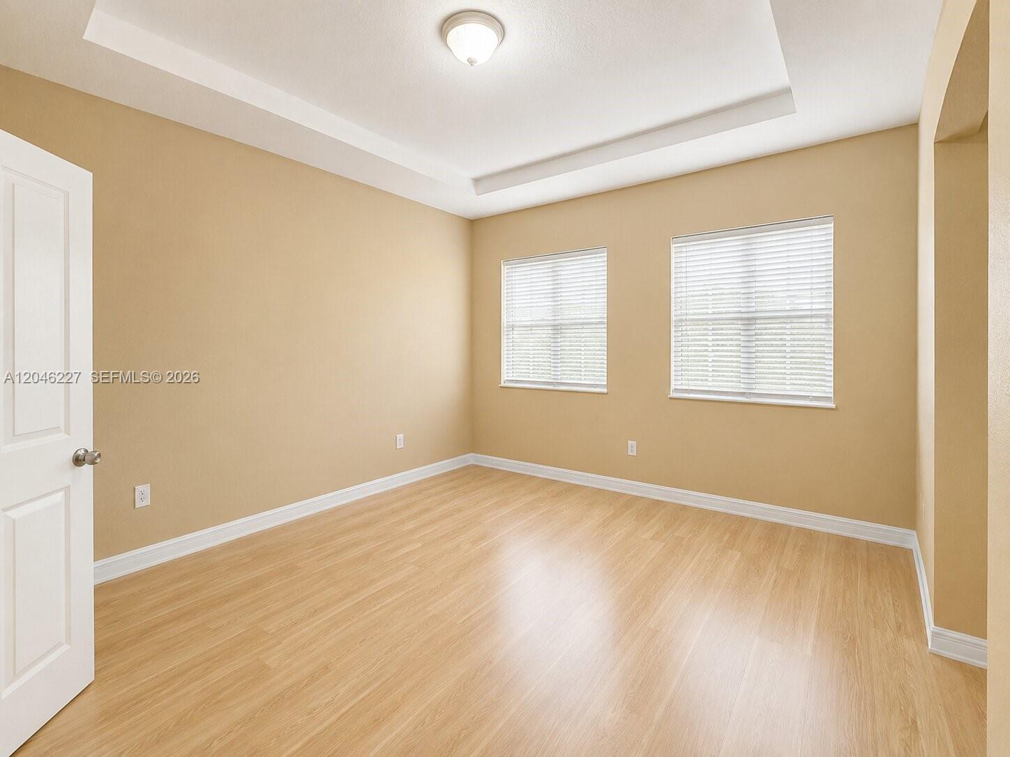 An empty room features light-colored walls, wood-look flooring, two windows with blinds, and a tray ceiling — 8526 NW 107th Psge # 40, Doral FL 33178, DORAL, FL