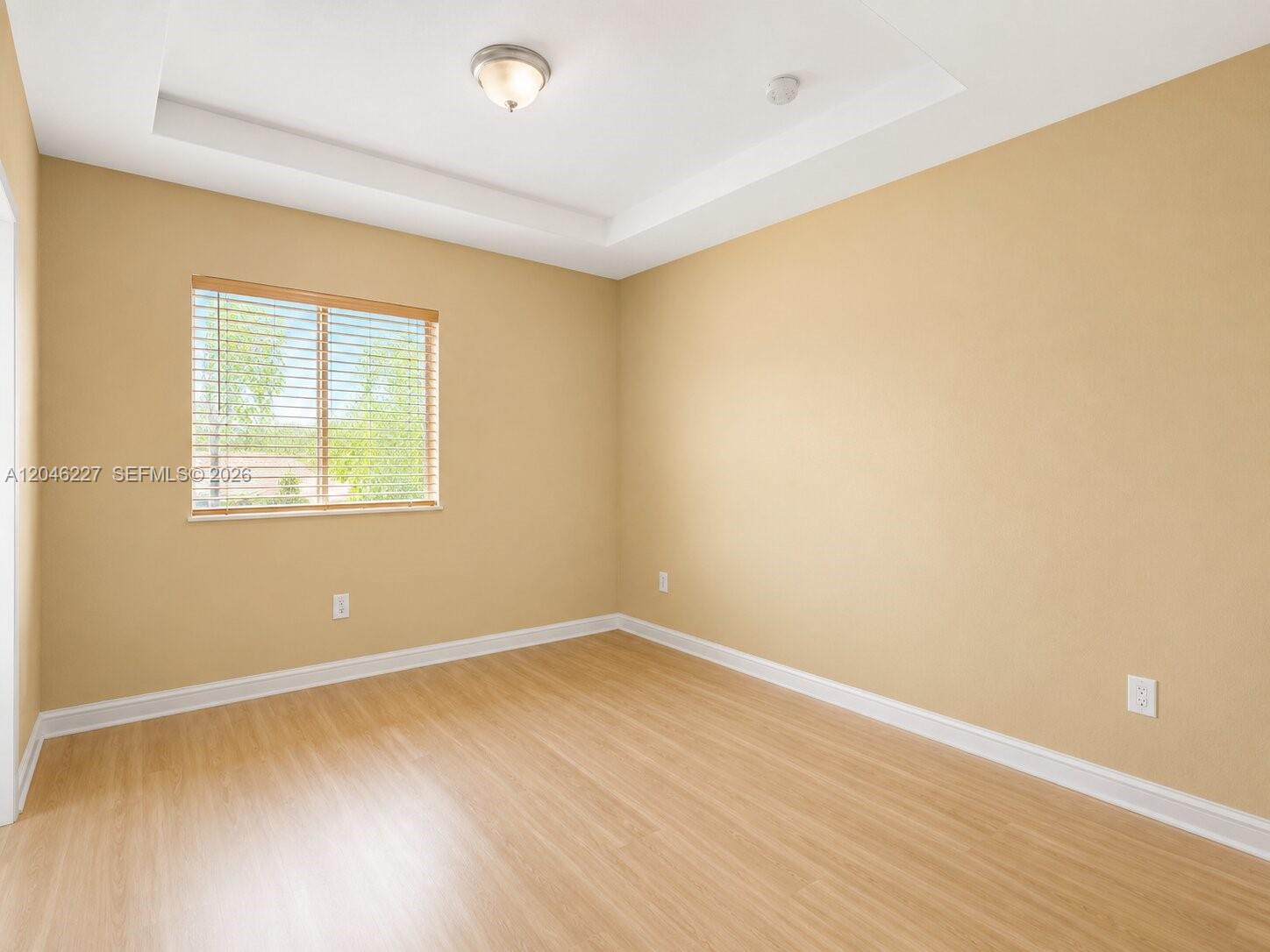 An empty bedroom features light-colored walls, wood-look flooring, a tray ceiling, and a window — 8526 NW 107th Psge # 40, Doral FL 33178, DORAL, FL