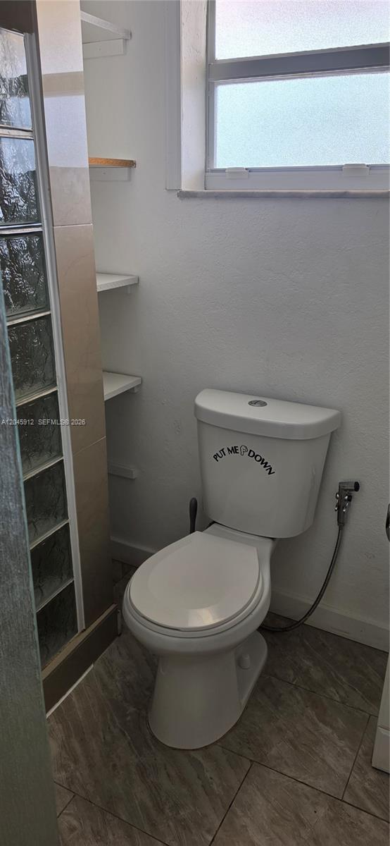 A bathroom features a toilet with a decal, glass block wall, and built-in shelving — AVENTURA, FL