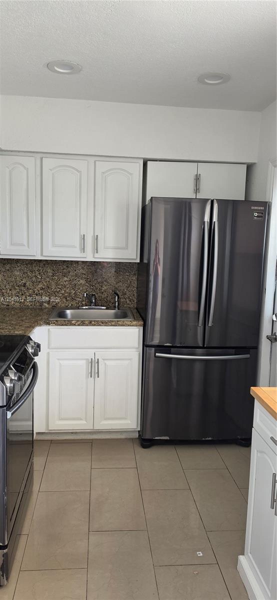A kitchen features white cabinets, granite countertops, a stainless steel sink, and a dark refrigerator — AVENTURA, FL