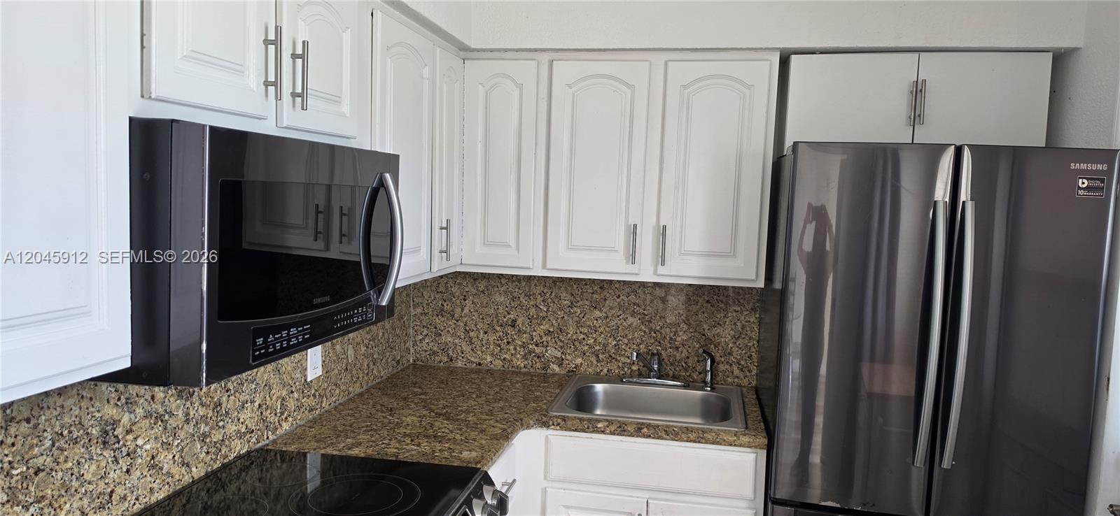 A kitchen features white cabinets, granite countertops, a stainless steel sink, and stainless steel appliances — AVENTURA, FL